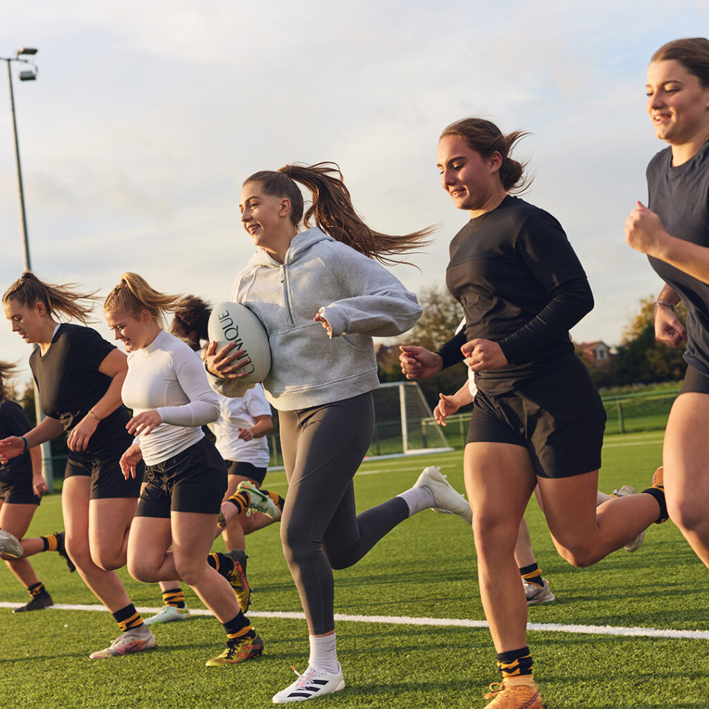 Holly Aitchison running on a rugby pitch with other female rugby players