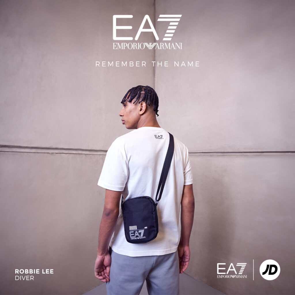 A young male athlete stands with his back to the camera wearing EA7 activewear, including a black side bag, with the EA7 logo overlaid along with the headline REMEMBER THE NAME
