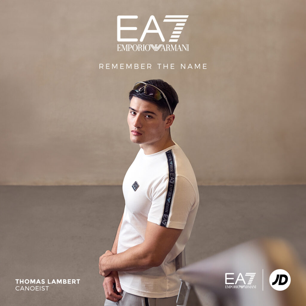 A young male athlete wearing EA7 activewear leans against the bannister of a staircase in an industrial off-white stairwell, with the EA7 logo overlaid along with the headline REMEMBER THE NAME