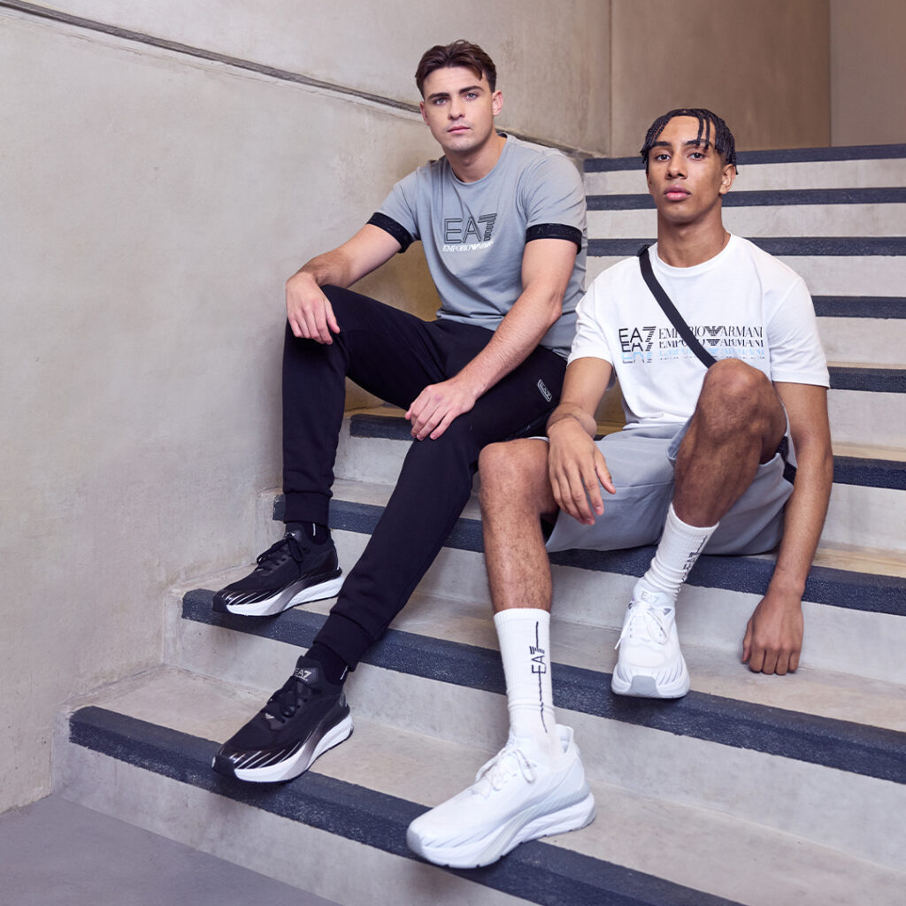 2 young male athletes wearing EA7 activewear sit on a staircase in an industrial stairwell