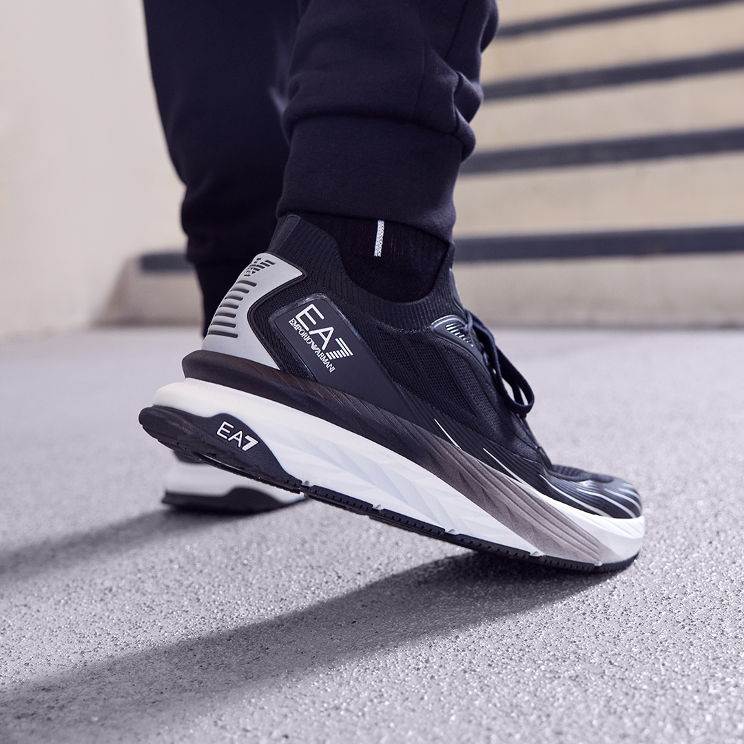 A close up of a black and white EA7 trainer on foot in an industrial stairwell