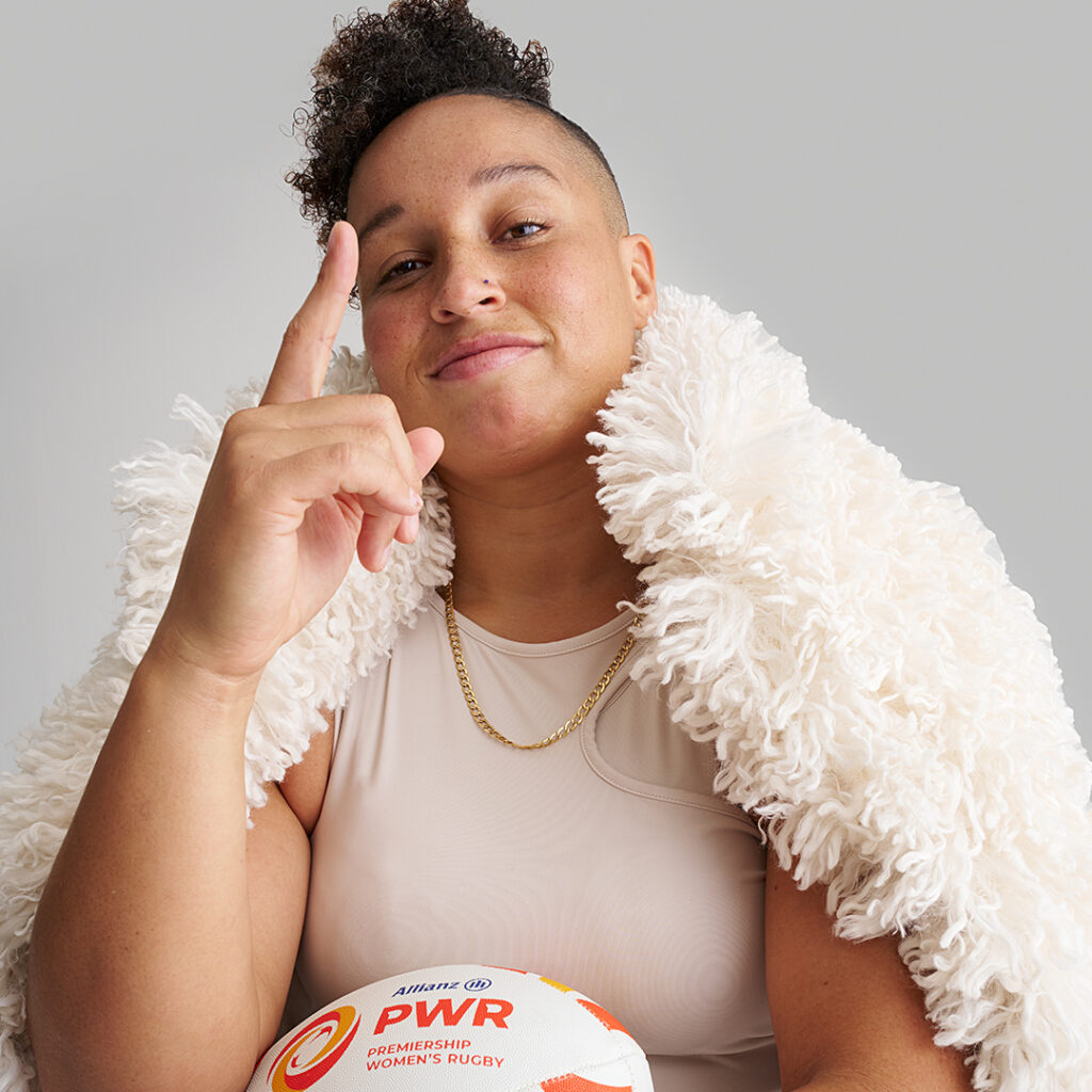 Shaunagh Brown posing with finger point up in front of a white backdrop, wearing a white shaggy coat