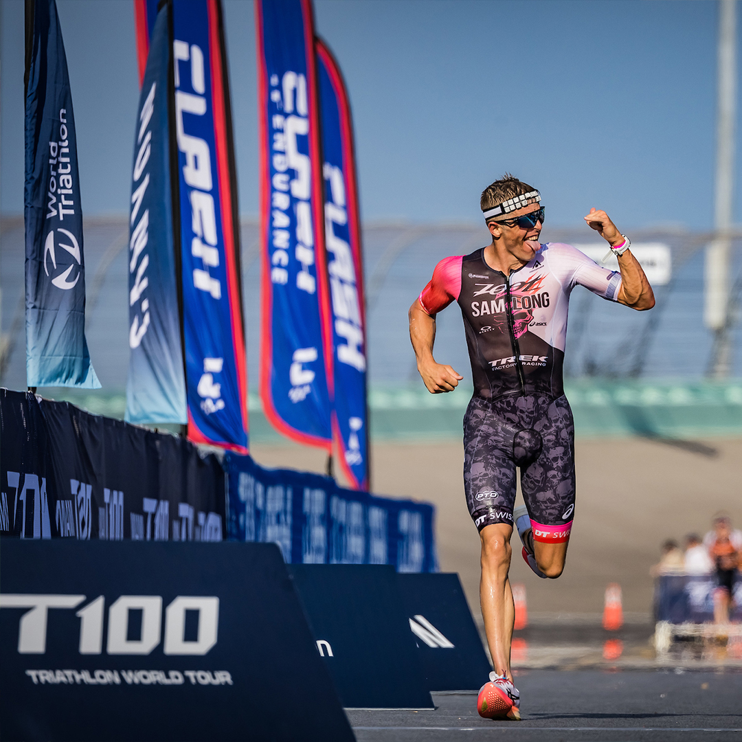 Athlete running in a race runs past T100 branded barriers and printed assets