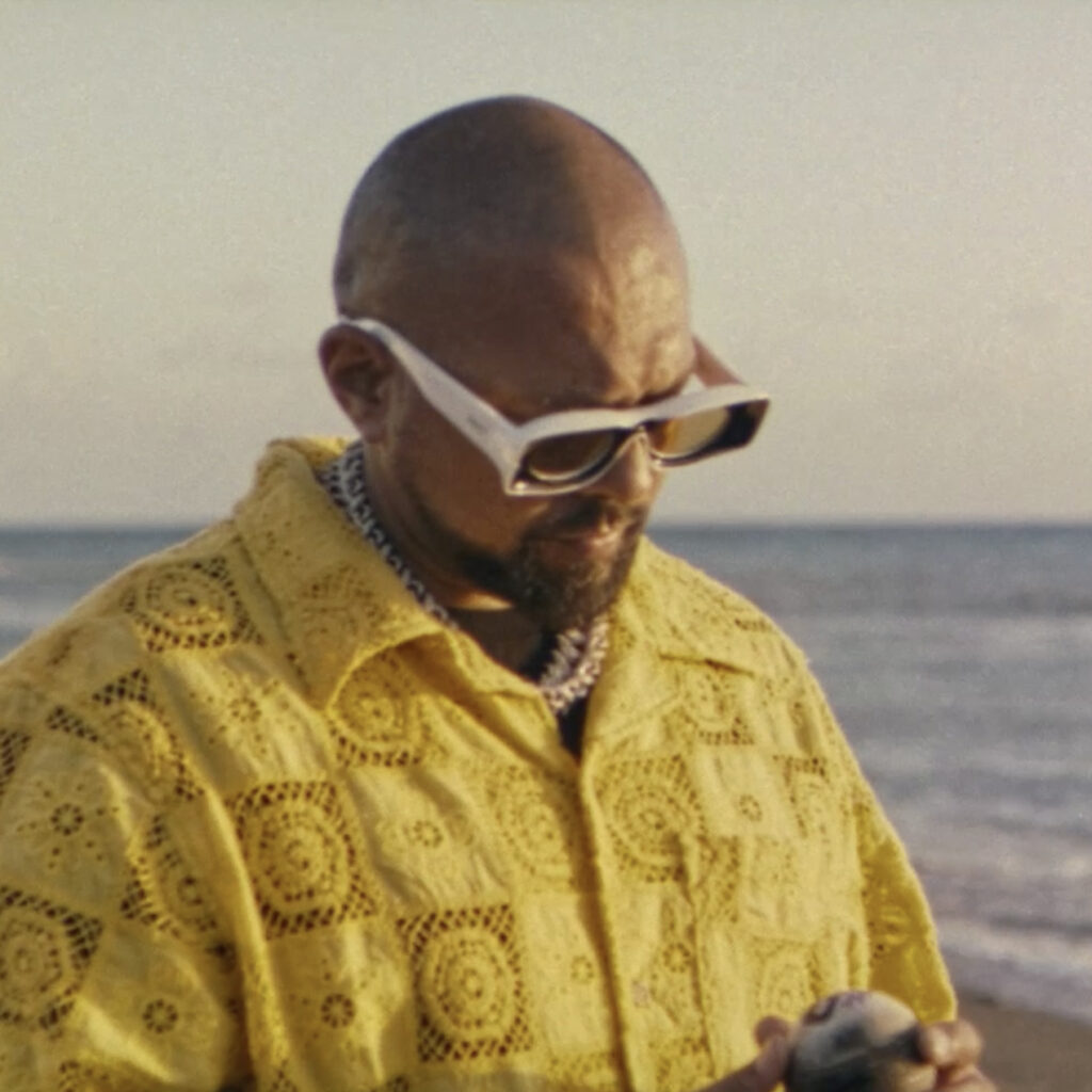 Sean Paul looking down at cricket ball on a beach in Out Of This World music video