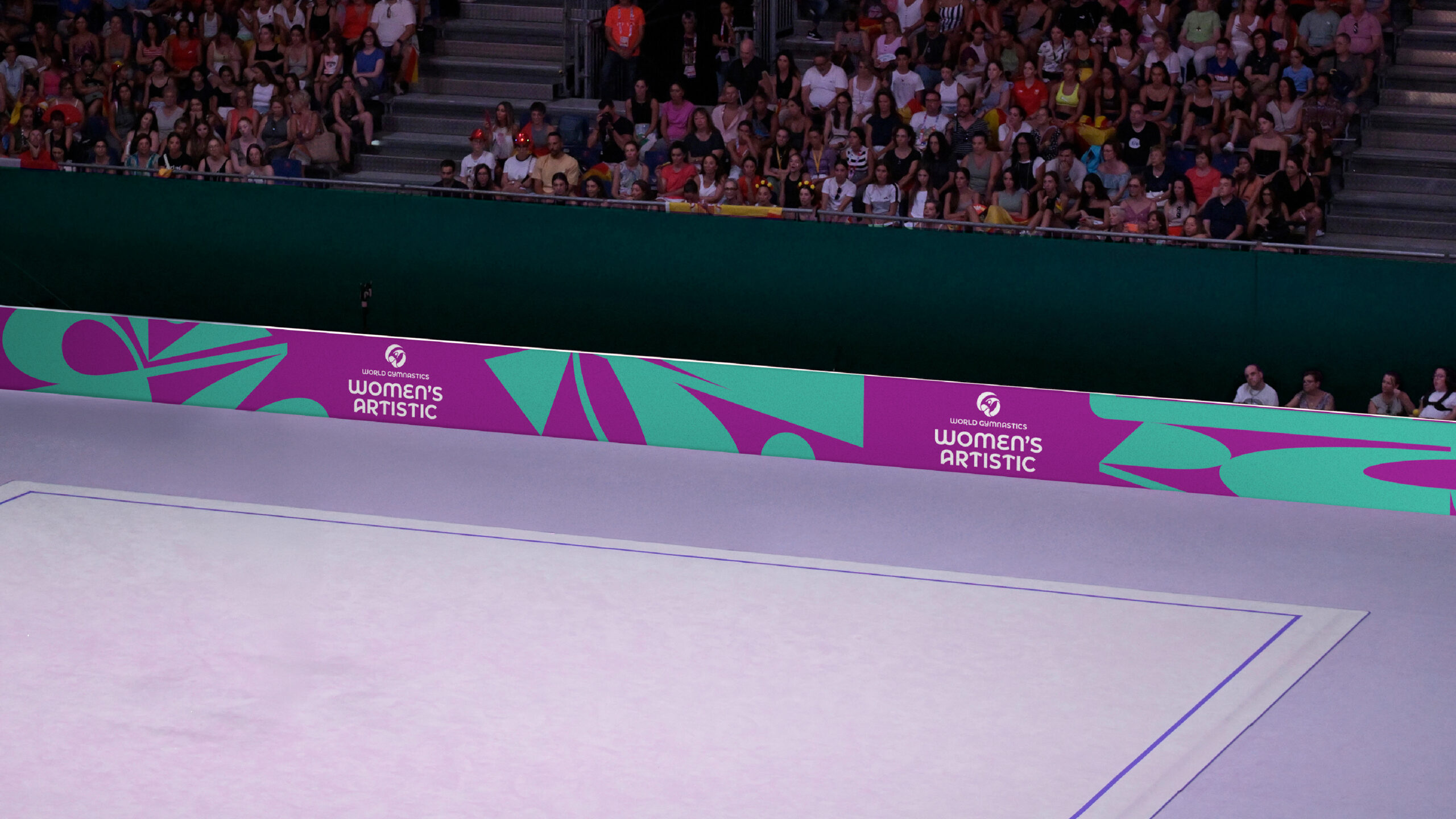 Mock up of World Gymnastics Women's artistic branded perimeter board as an event showing the floor in front of seated crowd