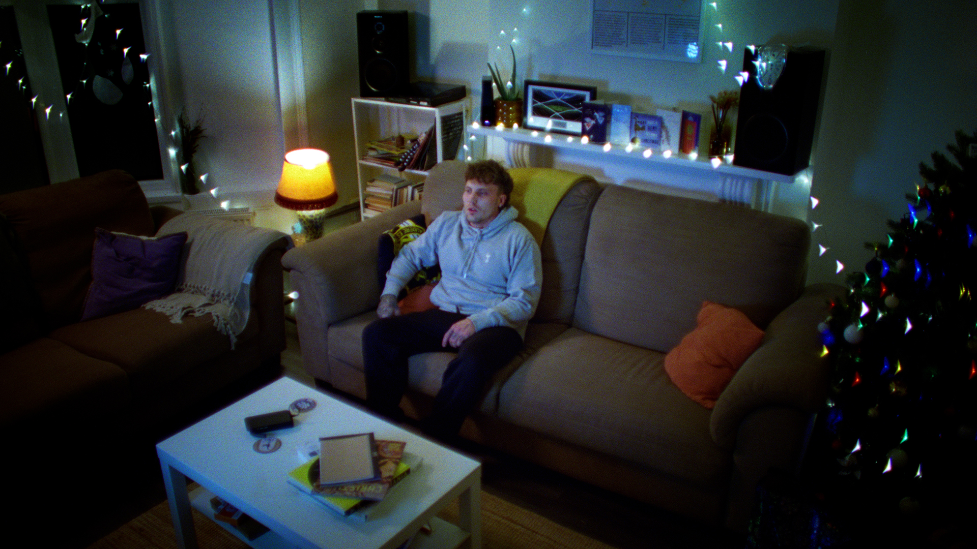 man in spurs hoodie sat on sofa in lounge next to christmas tree and christmas lights watching TV