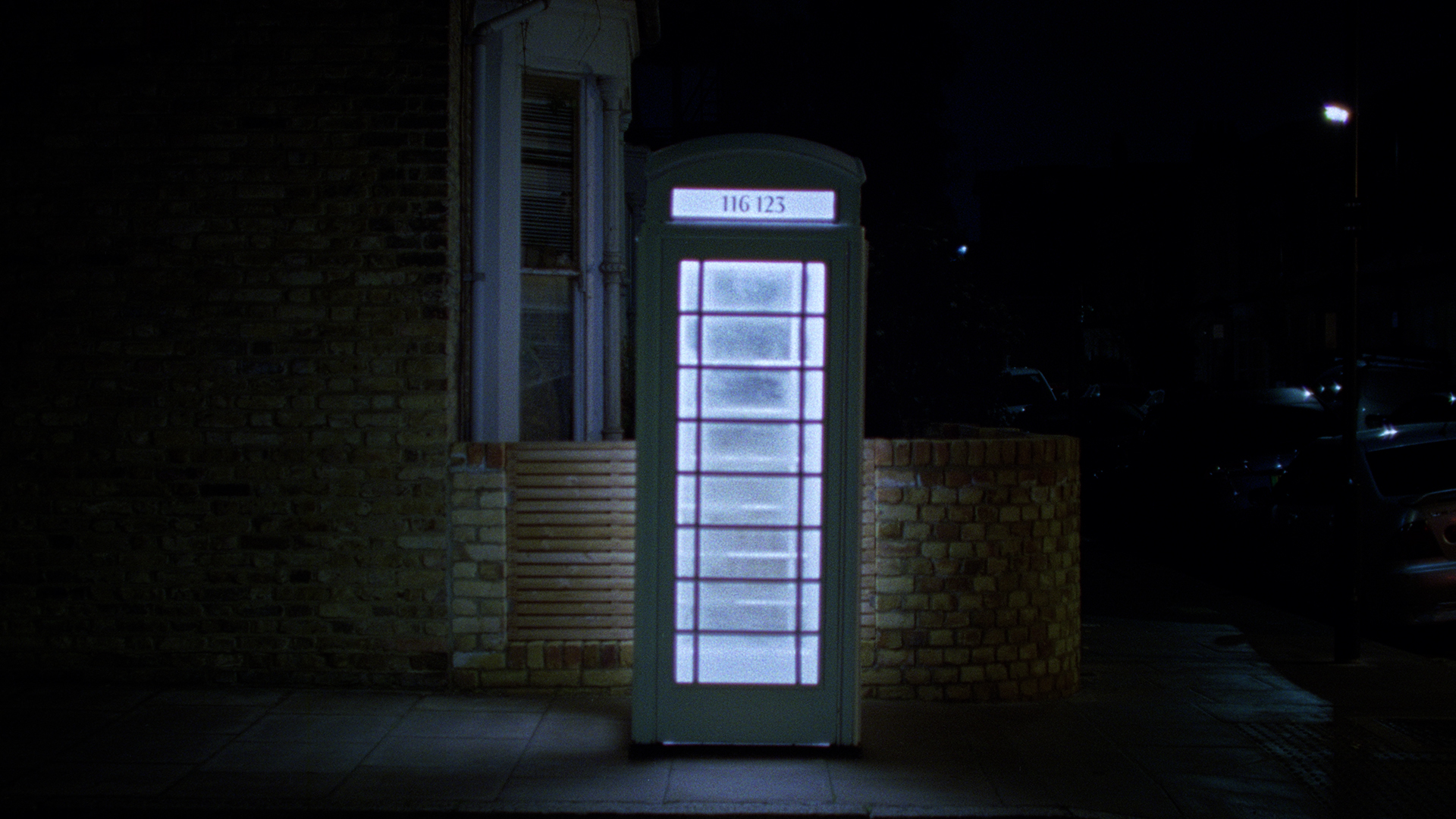 white phonebox on dark street corner lit up with Samaritans phone numbers on top panel